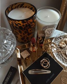 a table topped with candles and jewelry next to a glass bowl filled with lipsticks