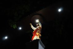 a statue of jesus on top of a pedestal in the dark with bright lights above it