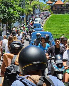 a large group of people riding scooters down a street next to a lush green field