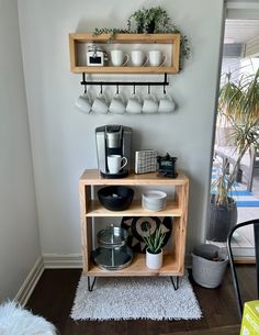 a shelf with cups and plates on it in the corner of a room next to a potted plant