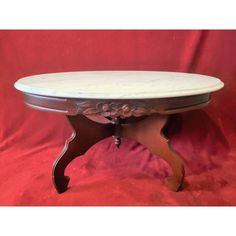 an oval marble top coffee table with wooden legs and carvings on the base, sitting against a red background