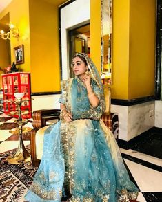 a woman in a blue and gold bridal gown sitting on a chair with her hand under her chin