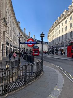 a red double decker bus driving down a street next to tall buildings