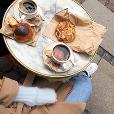 a person sitting at a table with two cups of coffee and pastries on it