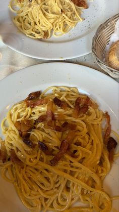 two white plates with spaghetti and bacon on them