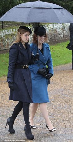 two women walking under an umbrella on a rainy day, one in blue coat and the other in black hat