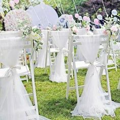 rows of white folding chairs decorated with flowers and ribbons for an outdoor wedding ceremony in the grass