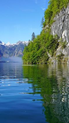 a body of water with mountains in the background and trees on both sides, surrounded by greenery