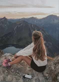 a woman sitting on top of a mountain next to a lake