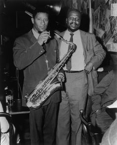 two men standing next to each other holding saxophones