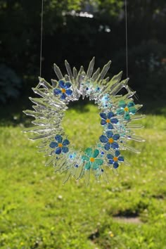 a glass sun catcher hanging on a string in the grass with trees in the background