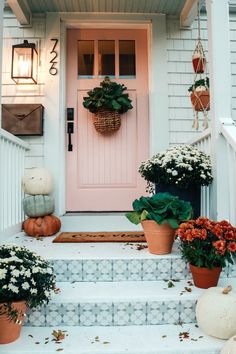 front porch decorated for fall with pumpkins and flowers on the steps, potted planters