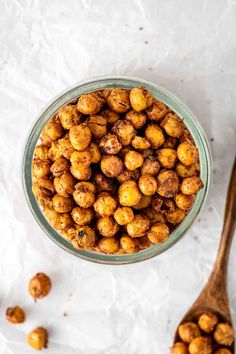 a glass bowl filled with chickpeas next to a wooden spoon on a white surface