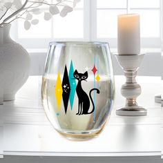 a wine glass with two cats on it next to a candle and some vases