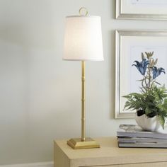 a lamp that is on top of a dresser next to a plant and pictures in a room