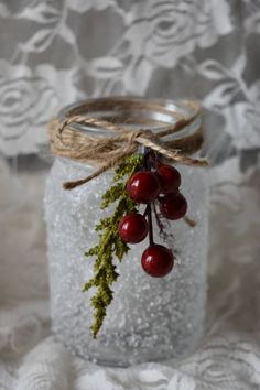 a glass jar with some berries hanging from it's side on a lace tablecloth