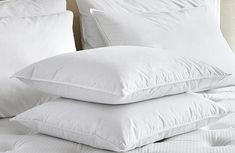 three pillows stacked on top of each other in front of a bed with white sheets