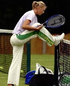 a female tennis player leaning on the net with her racket in hand while looking at her cell phone