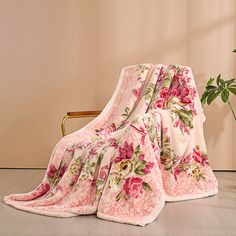 a pink flowered blanket sitting on top of a chair next to a potted plant