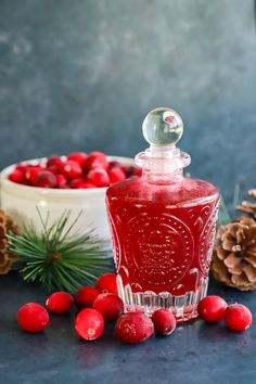 a bottle of red liquid surrounded by berries and pine cones