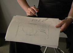 a person sitting in a chair holding a piece of paper with a drawing on it