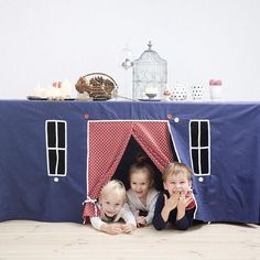 three children laying on the floor in front of a blue tent with red and white polka dots