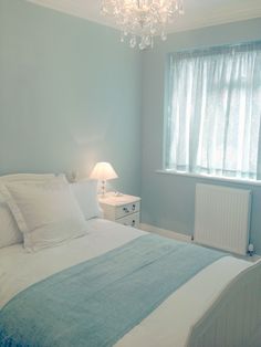 a bedroom with blue walls and white bedding has a chandelier hanging from the ceiling