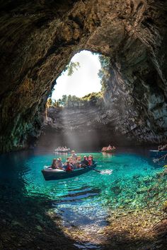 several people are in a small boat near the entrance to a cave with blue water