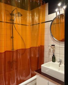 an orange shower curtain in a bathroom next to a white sink and mirror with lights on