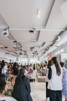 a large group of people are sitting and standing in a room full of chairs, looking at each other