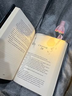 an open book sitting on top of a bed next to a pink toy bear and lamp