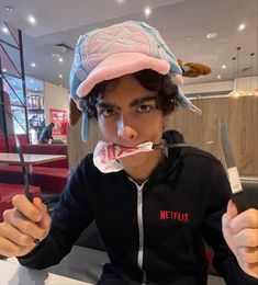 a man in a pink hat is holding a knife and fork with food on it