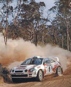 a car driving down a dirt road with dust coming out of the front window and trees in the background