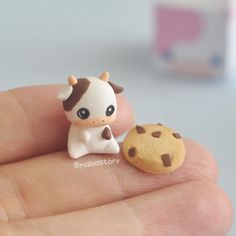 a tiny cow figurine sitting next to a cookie on someone's finger