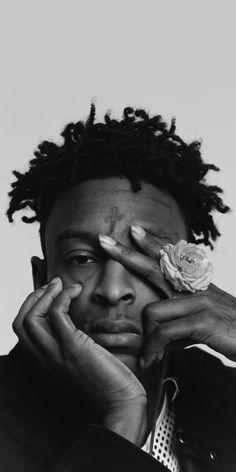 a black and white photo of a man with dreadlocks holding a rose in his hand