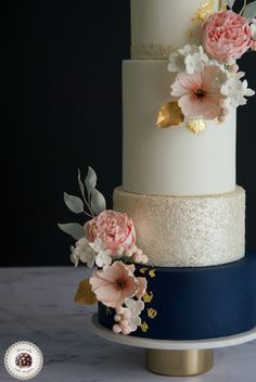 a three tiered wedding cake with pink flowers on top and blue ribbon around the bottom