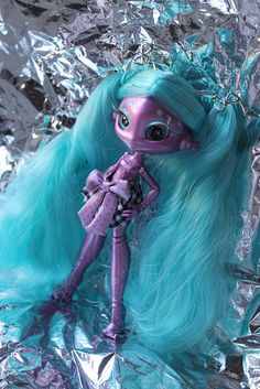 a close up of a doll with blue hair and green eyes on tinfoiled surface