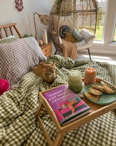 a cat laying on a bed next to a table with food and drink in front of it