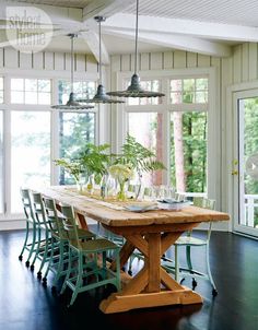 a dining room table with chairs and plants on it in front of large windows that look out onto the woods