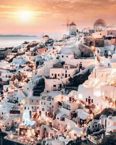 an aerial view of the white city of oia at dusk, with windmills in the background