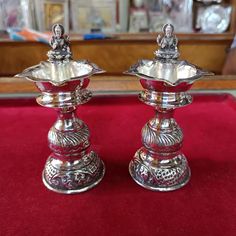 two silver candlesticks sitting on top of a red table