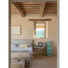 a bed sitting under a window next to a table and chair in a room with wooden beams