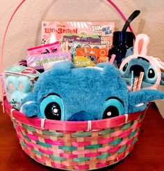 a blue stuffed animal sitting in a basket filled with books and toys on top of a wooden table