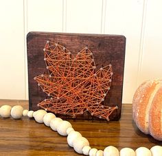 a wooden board with string art on it next to some white balls and a pumpkin