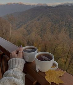 two cups of coffee sitting on top of a wooden table next to a person's hand