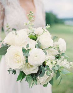 a bridal holding a bouquet of white flowers and greenery in her hands,