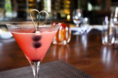 a pink drink with blueberries in it sitting on a wooden table next to wine glasses