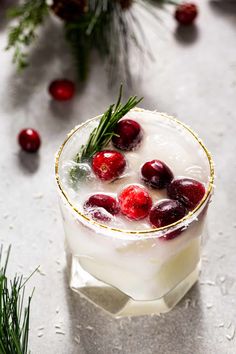 a drink with cranberries and rosemary garnish in a glass on a table