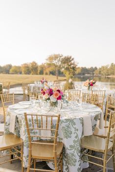 an outdoor table set up with chairs and tables covered in floral centerpieces for a wedding reception