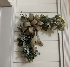 a wreath is hanging on the wall next to a door with green leaves and greenery